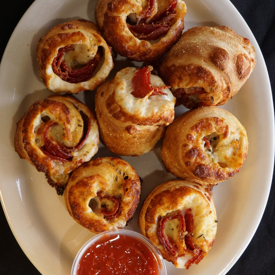 A plate of golden-brown pepperoni and cheese pizza rolls with a side of marinara sauce.