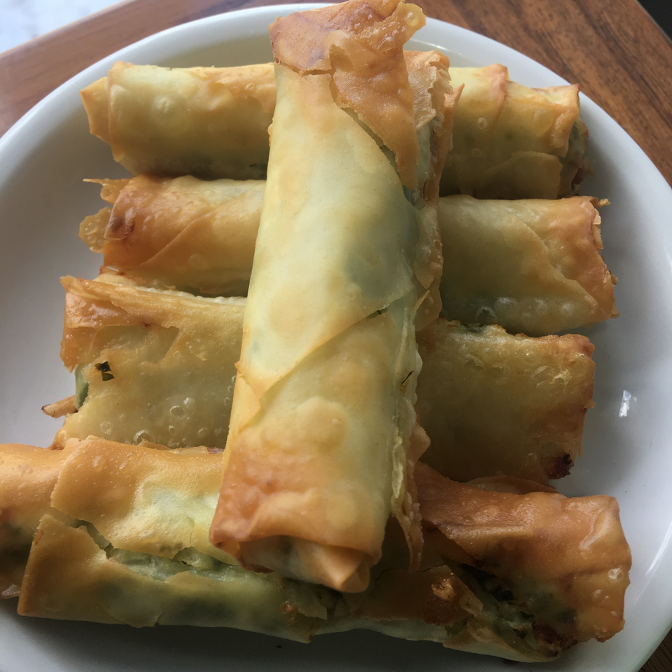 A white bowl filled with golden-brown, crispy spring rolls, some stacked vertically.