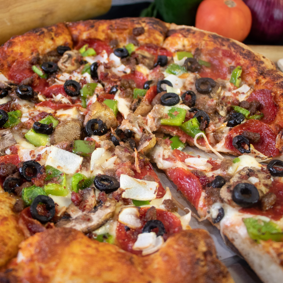A close-up of a fully loaded Uptown Kitchen Pizza with pepperoni, sausage, olives, and peppers.